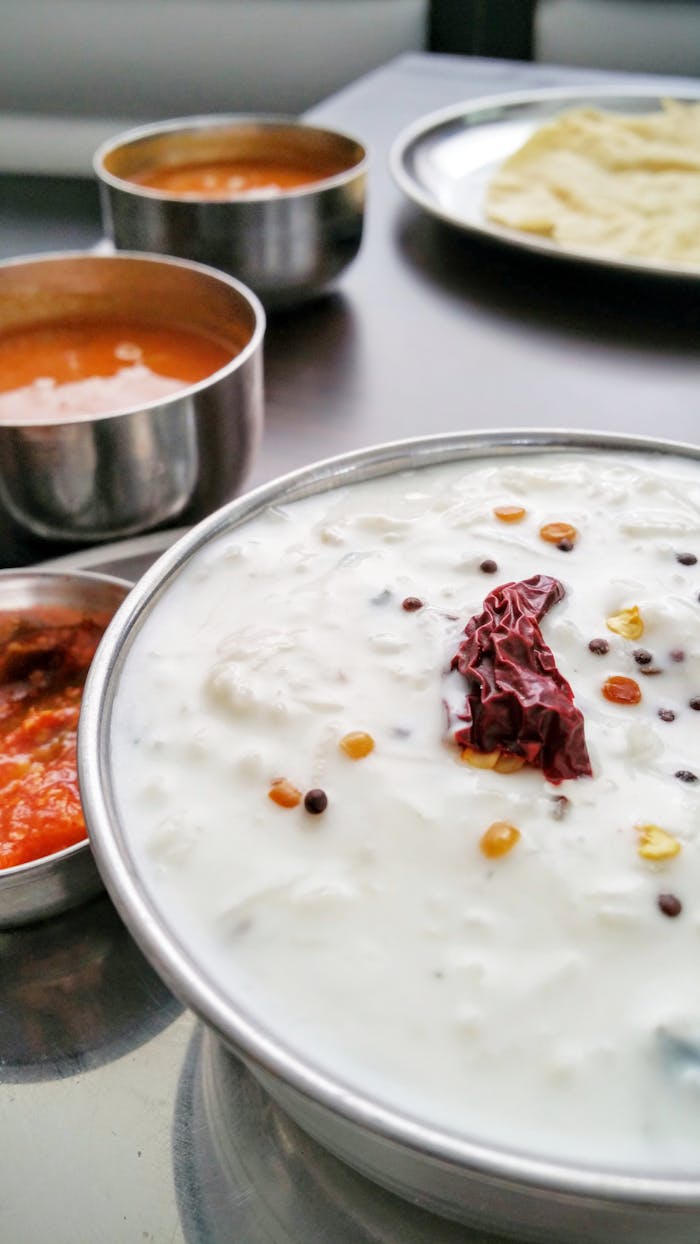 services-03 A vibrant spread of Indian dishes featuring yogurt raita, spicy curries, and flatbread on a stainless steel plate.