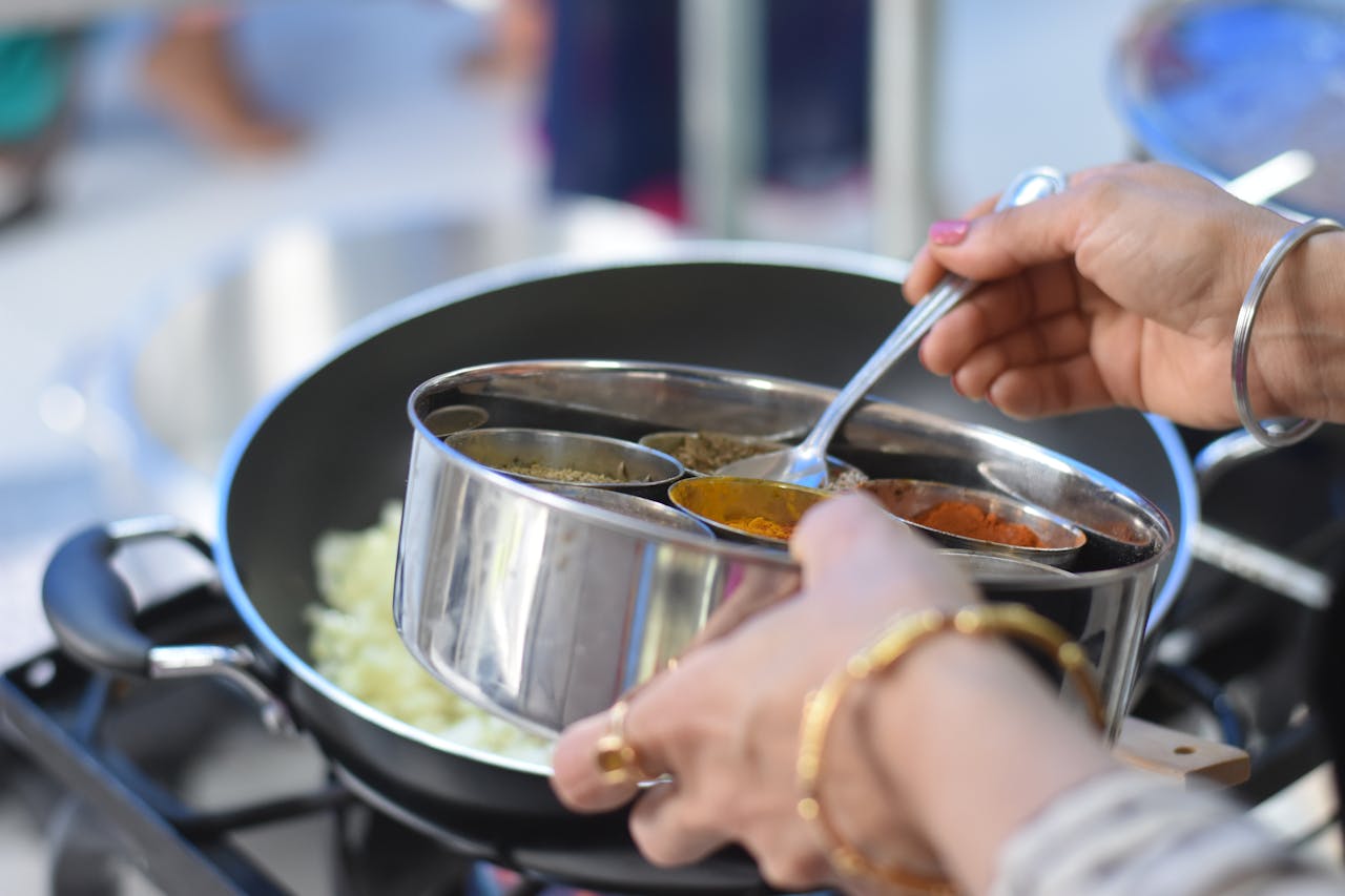 services-01 Close-up of hands preparing Indian dish with spices in a cooking pan.
